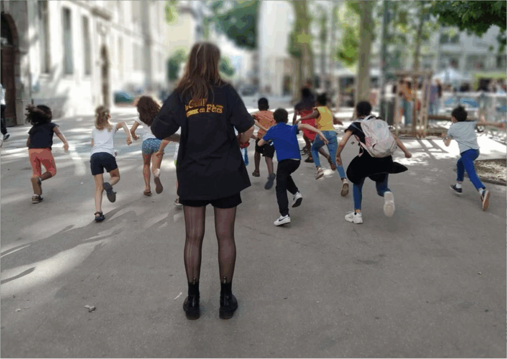 Enfants courant dans une cour de récréation avec un adulte de dos au premier plan